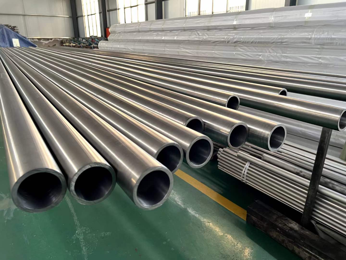 A range of titanium tubes of various diameters and lengths displayed in a modern Chinese factory workshop